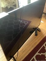 Front right angle view of TV on stands showing screen and remote on floor