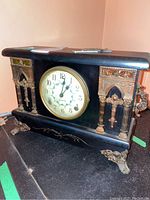 Front view of the black wood mantle clock with metal decorative accents and visible dial showing brand Sessions.