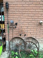 Two rusty metal wagon wheels leaning against brick wall with tiki light and weather vane behind