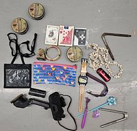 Overview of assorted vintage and modern items including playing cards, watches, jewelry, and small personal items on a gray floor.