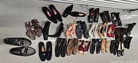 Overhead view of assorted men's and women's shoes arranged in rows on the floor, showing various styles including loafers, high heels, ankle boots, and flats.