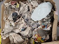 Top view of box showing assorted glassware and a white ceramic or porcelain serving platter among crumpled newspaper inside a cardboard box.