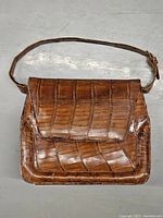 Front view of vintage brown alligator leather purse with flap and shoulder strap laid flat