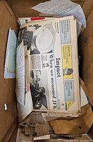 Stack of vintage newspapers and documents in a box featuring a headline about mourning JFK