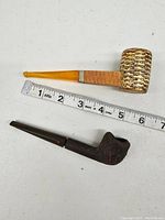 Two vintage pipes including a yellow acrylic mouthpiece corn cob pipe and a dark wood pipe next to a measuring tape showing approximately 6 inches length for the corn cob pipe.