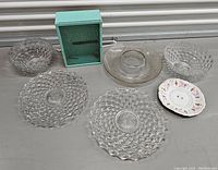 Photo showing six pieces of clear glass servingware with one small floral porcelain dish along with a teal wooden vintage shadowbox frame.