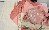 Group view of vintage fabrics showing cream-colored tablecloth, pink fabric with fringe, rolled pink floral damask fabric, and floral printed beige fabric.