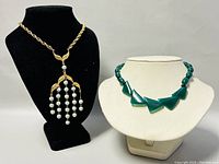 Two necklaces displayed on bust forms: left is a 20-inch gold-toned D’ORLAN necklace with dangling pearl-like beads and leaf design, right is a 14-inch green beaded choker with triangular beads.