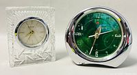 Two vintage alarm clocks on white surface: clear faceted cut crystal Belfor clock on left, round green faced metal alarm clock on right