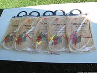 Five packages of Vorax-Vino extendable siphon hoses laid on white table outdoors on grass background. Each package includes a white translucent flexible hose coiled inside an unopened transparent plastic bag with printed red grape design and text.