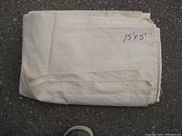 Folded off-white canvas drop sheet with stitched edges and hand-labeled dimensions '15'x5' on surface, laid on pavement.