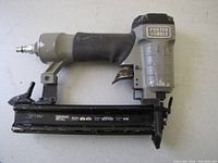 Photo of a Porter Cable 18 gauge brad air nailer with a gray and black finish, showing the grip handle, air hose connection, and nail magazine.
