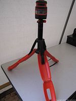 Laser level mounted on orange tripod with legs spread out on a table indoors.
