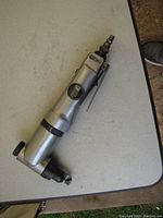 Power Fist air nibbler placed on a white surface, showing the full body including air connector, lever trigger, and branding on the side.