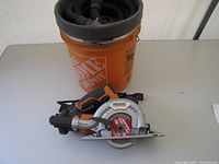 Photo showing the Ridgid fiber cement saw, vacuum hose coiled on top of an orange Home Depot branded bucket.