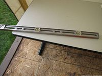 Heavy aluminum 4-foot spirit level with three bubble vials placed on a beige folding table indoors.