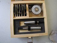 Metal circular cutting discs, two shaft components, and assorted washers in a foam-lined wooden box