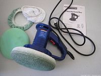 Blue Simoniz 8 inch random orbit polisher with attached cleaning pad, two extra cloth pads, a green foam pad, and instruction manual laid out on a surface.