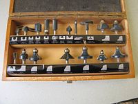 Wooden box holding 16 Mastercraft router bits with 1/4 inch shank. The bits are arranged in two rows with labels showing profiles.