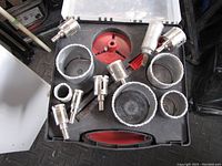 Metal diamond tip hole saw cutting bits arranged inside a black hard plastic carrying case with red interior. Various sizes from small to large diameters included.