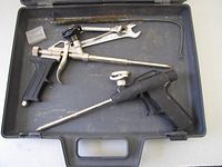 Two large canister spray foam tools and various cleaning accessories arranged inside an open black carrying case on a white surface.