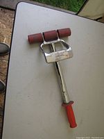Photo of Roberts 7 inch tile roller showing metal frame, three red rubber rollers, telescoping metal handle with red plastic grip, placed on a table.