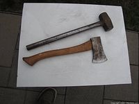 Photo showing one small sledge hammer with metal handle and one small axe with wooden handle on white surface
