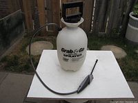 White 1 gallon Grab & Go sprayer on white table outdoors. Shows full view of sprayer including handle, pump, and nozzle.