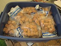 Plastic bin filled with many sealed packages containing 12 natural corks each. The corks are light brown and shaped for inserting into gallon jug necks.