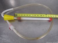 Extendable siphon hose with yellow funnel end, clear flexible tubing, white inner tube, and red shut off valve beside a measuring tape showing length.