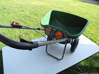 Side angle of green Scotts Deluxe spreader showing handle, dial, and hopper