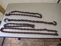 Photo showing three heavy metal chains of varied lengths with hooks placed on a table.