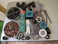 Displayed assortment of plumbing fittings and parts including elbows, connectors, hoses, caps, and covers on a table.