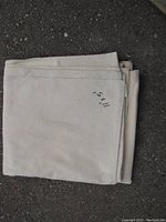 Folded off-white painters drop sheet, edges hemmed, with a handwritten marking indicating dimensions.