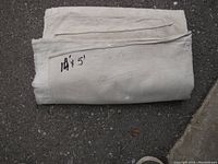 Folded off-white painter's drop sheet laid on asphalt with '14 x 5' marked on it.