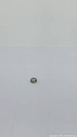 Photo of the loose oval cut green sapphire gemstone on a white background showing its color and shape.
