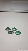 Four natural forest green polished malachite gemstones showing various shapes and natural banded patterns.