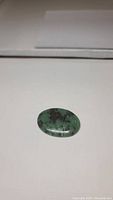 Oval polished cabochon ruby zoisite gemstone showing green zoisite with ruby inclusions on a white background