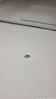 Image of a marquis cut apple green peridot gemstone on a white surface showing its size and color.