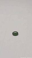 Photo of the oval cut green chrome diopside gemstone lying flat on a white surface showing faceting and color tone