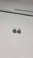 Pair of small round natural emerald stud earrings with faceted stones set in sterling silver.