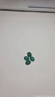 Four natural green onyx oval cabochon gemstones arranged in a cluster on white background.