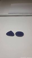 Two polished gemstones of natural lapis lazuli, deep blue color, triangular and oval shapes.