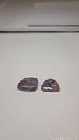 Two natural purple charoite stones laid flat on white surface, showing polish and natural patterns
