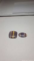 Two polished natural purple fluorite cabochon gemstones on white background showing color zoning and translucency