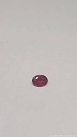 Oval cut natural ruby gemstone approximately 7x5mm size showing deep red color and clarity enhanced features.