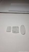 Three natural selenite crystals displayed side by side on a white surface, highlighting the shape and texture of the stones.