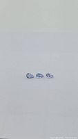 Three pear-shaped natural blue-purple tanzanite gemstones placed in a row on white background