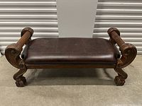 Full front view of antique leather bench showing seat and carved wooden legs and armrests
