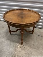 Three-legged antique wooden side table with scalloped circular top and carved connecting stretchers